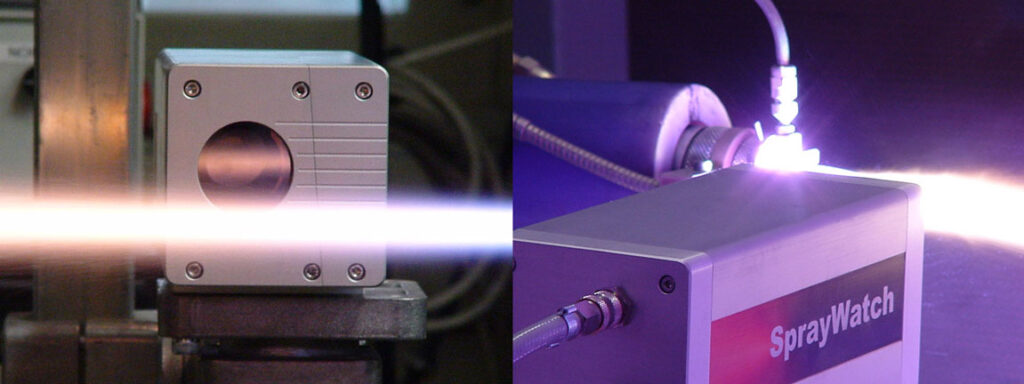 A bright horizontal laser beam passes between two industrial machines, with a purple-lit unit labeled SprayWatch on the right.