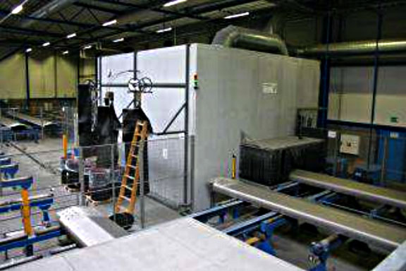Industrial workshop featuring a large gray machinery enclosure, yellow ladder, and blue conveyor rails.