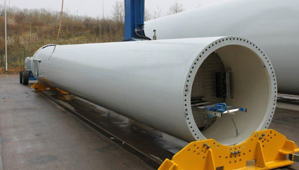 Large white cylindrical wind turbine tower section with a bolted end flange in an outdoor industrial yard.