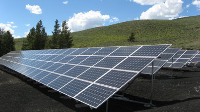 Ground-mounted solar panels arranged in rows across a rural landscape with hills and trees.