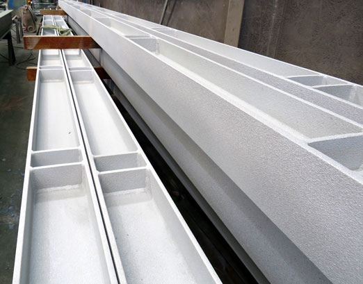 Several long white aluminum extrusion profiles with hollow rectangular sections stacked in a workshop.