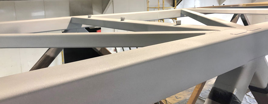 Close-up of light-gray metal beams forming a geometric framework in a workshop.