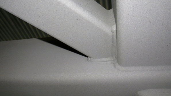 Close-up of a white panel with a small seam and a dark crevice, with a ribbed grille visible in the background.