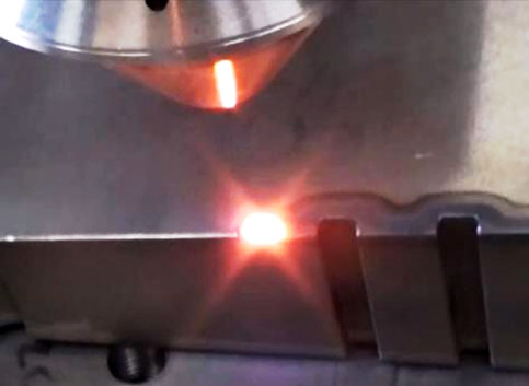 Close-up of a metal tool with a small bright red light against a gray surface.
